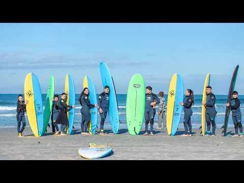 Family Circle participants in wetsuits gather with colorful surfboards on a beach.