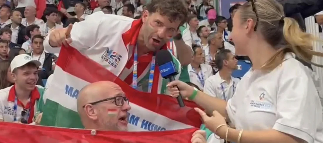 A reporter interviews supporters holding flags in the stands at the Maccabiah Games.