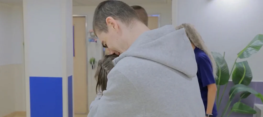 Maxim Herkin embraces a woman in a hallway.