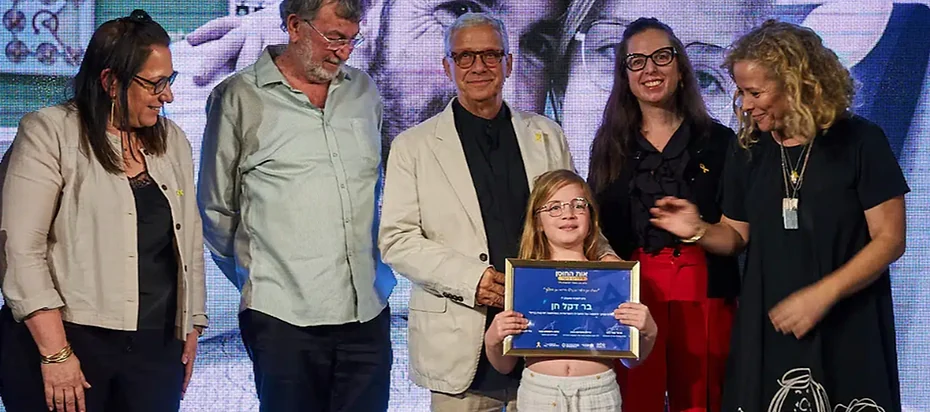 A young Resilience Award recipient holds her award alongside presenters on stage.
